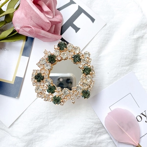 Flat lay of a luxury gold crystal phone grip with green rhinestones and a mirror center