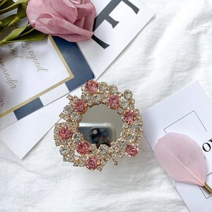 Close-up of a pink rhinestone-studded phone grip with built-in mirror on a decorative cloth