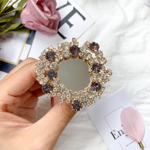 Detail of a round gold mirror phone socket with purple and white crystals held in hand