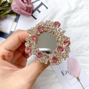 Detail of hand holding a luxury gold mirror phone grip with pink and white rhinestones