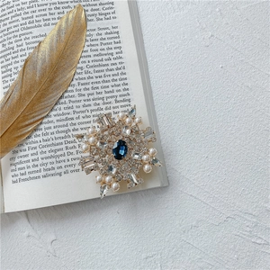 Dettaglio della spilla a fiocco di neve con gemma blu e perle su un libro d'epoca