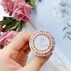 Detail eines rosa Glitzer-Handyhalters mit weißen Kunstperlen und Je T'aime-Schriftzug