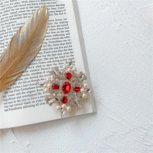 Dettaglio spilla barocca vintage con pietre rosse e perle bianche su un libro aperto