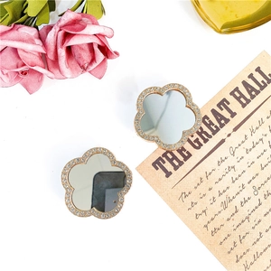 Detailed close-up of two rhinestone clover mirror phone grips on vintage paper background