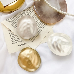 Detailed view of irregular hammered metal ear studs in gold and silver on a silk background