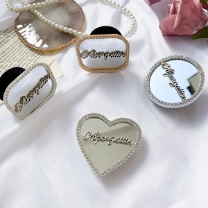 Close-up of heart and round rhinestone phone grips with mirrors on white silk