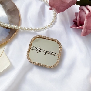 Detail of square vanity mirror phone stand with gold rhinestones and metal letter decoration