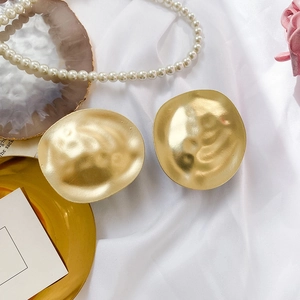 Macro detail of large golden irregular earrings with hammer-textured finish on silk fabric