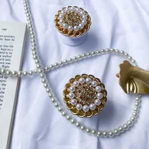 Detail of luxury pearl and rhinestone sunflower phone grip on white silk background