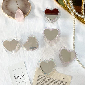 Détail de supports de téléphone cœur avec paillettes et miroir sur tissu blanc
