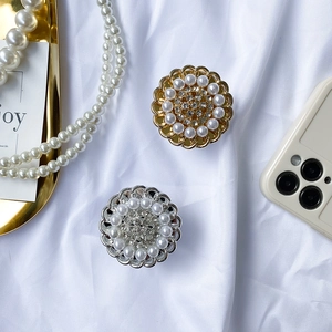 Close-up of luxury flower-shaped phone grips with rhinestones and pearls on white silk