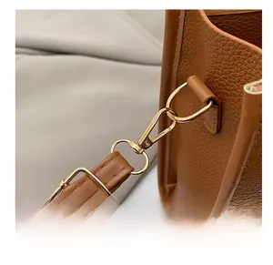 Close-up of golden metal hooks and adjustable buckle on brown lychee texture leather bag
