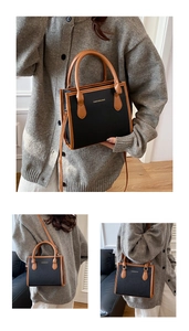 Detail of black faux leather crossbody bag with brown handles and gold lettering