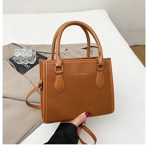 Detail of tan pebble leather handbag featuring gold Fashion & Bag lettering and handles