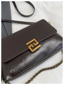 Détail du sac à bandoulière en cuir marron foncé avec boucle dorée et texture plissée