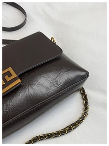 Détail d'un sac porté épaule en cuir froissé marron foncé avec boucle dorée et chaîne