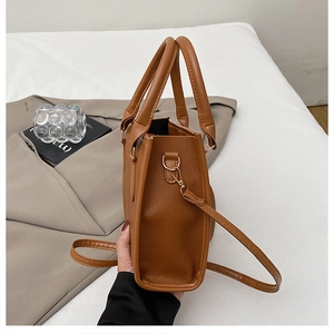 Detail view of brown lychee texture leather handbag with gold hardware and top handle