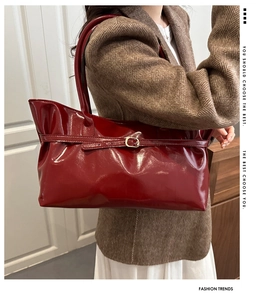 Deep burgundy patent leather bucket bag with decorative belt detail shown as underarm tote