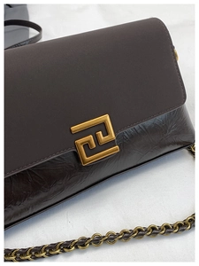 Détail de la texture cuir marron foncé et boucle géométrique dorée sur le sac à bandoulière