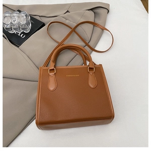 Detail of brown litchi pattern PU leather handbag with dual handles and metal buckles