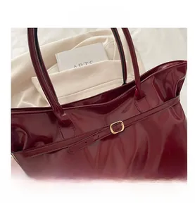 Detail of burgundy glossy patent leather tote bag with elegant gold buckle hardware