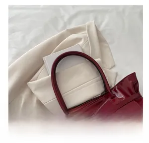 Close-up of glossy wine red patent leather tote bag with stylish metallic buckle straps