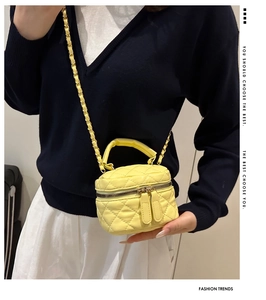Detail of yellow quilted box bag showing golden hardware and metal chain strap