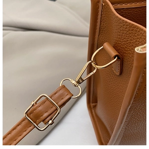 Detailed close-up of brown pebble leather texture and gold metal hardware on the handbag