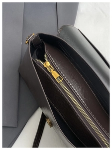 Détail d'un sac bandoulière en cuir marron foncé avec fermeture éclair dorée et aimantée