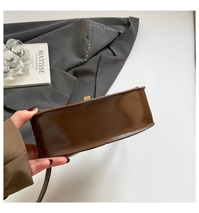 Detail of glossy dark brown semi-circular handbag with high-shine leather texture