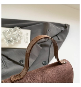 Detail of a brown suede handbag showing shiny patent leather handles and fine stitching