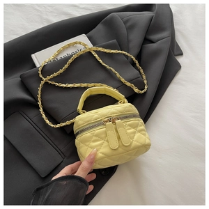 Detail of yellow quilted mini box bag with chain strap against a black blazer background