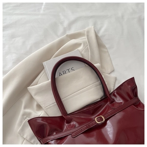 Detailed view of glossy burgundy tote bag with gold buckle on white textured fabric