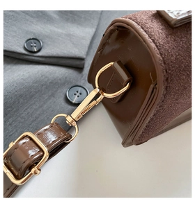 Detail of brown cylinder bag showing stitching, gold metal buckles, and suede texture