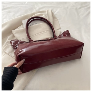 Detail of burgundy glossy leather tote bag showing shiny texture and gold metal buckle