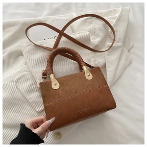 Detail of caramel leather crossbody bag with woven handle and suede patchwork on fabric
