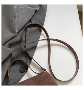 Detail of dark brown matte crossbody bag with slim strap next to a grey blazer