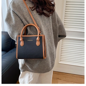 Detail of a two-tone black and brown lychee grain tote bag with gold fashion text