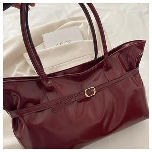 Detail of burgundy patent leather tote bag with gold metal buckle and leather strap