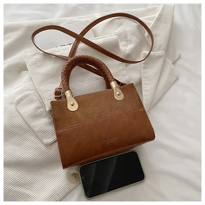 Detail of a brown leather crossbody bag with woven handles and golden hardware