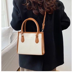 Detail of white lychee leather tote bag with brown handles on a black blazer