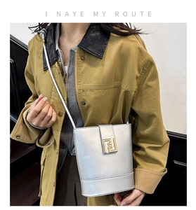 Chic silver matte bucket bag with golden geometric clasp detail on khaki jacket