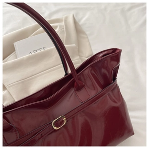 Close-up of glossy burgundy tote bag with gold metal buckle and shiny patent leather texture