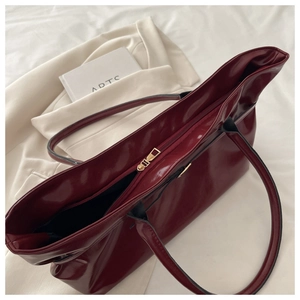 Detail of burgundy patent leather tote bag showing glossy texture and gold zipper closure