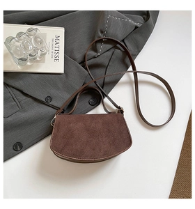 Detail of a dark brown suede semi-circular crossbody bag on a minimalist background
