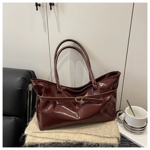 Close-up of burgundy glossy leather tote bag with gold buckle on a knitted scarf