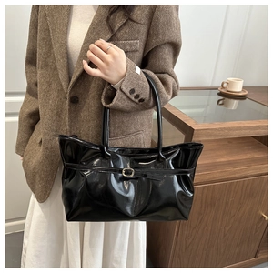 Detail of glossy black tote bag with gold buckle strap on model in brown blazer
