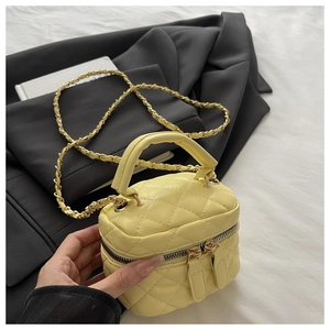 Detail of yellow quilted leather vanity bag with chain strap and top handle against black blazer