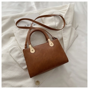 Detailed macro view of woven leather handle and gold hardware on brown crossbody bag