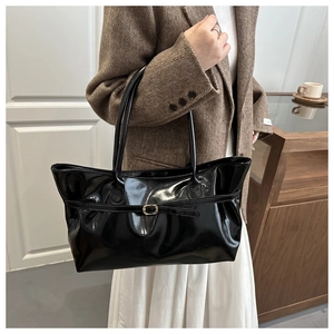 Detail of glossy black tote bag with gold buckle on a stylish model in modern interior